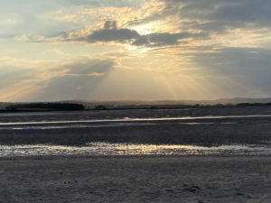The setting sun shines through the clouds over Budle Bay, Northumberland
