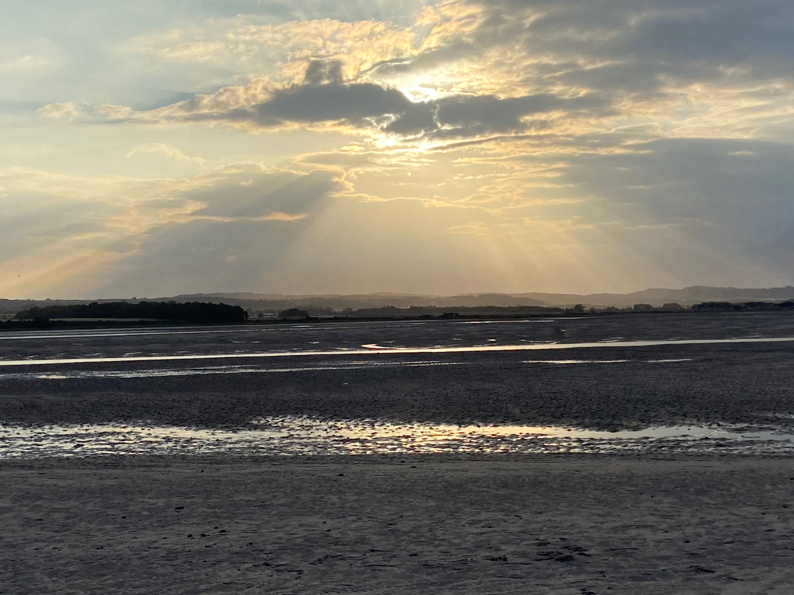 The setting sun shines through the clouds over Budle Bay, Northumberland